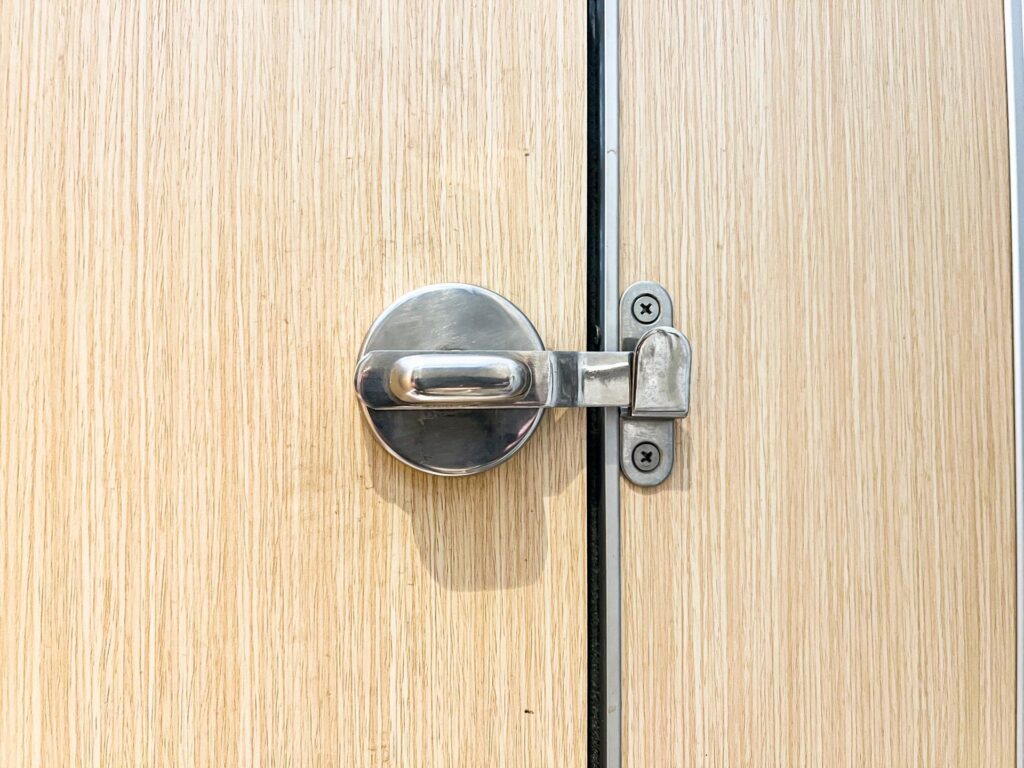 Minimalist stainless steel door latch on a wood-textured door, great for architecture, home improvement, and security topics