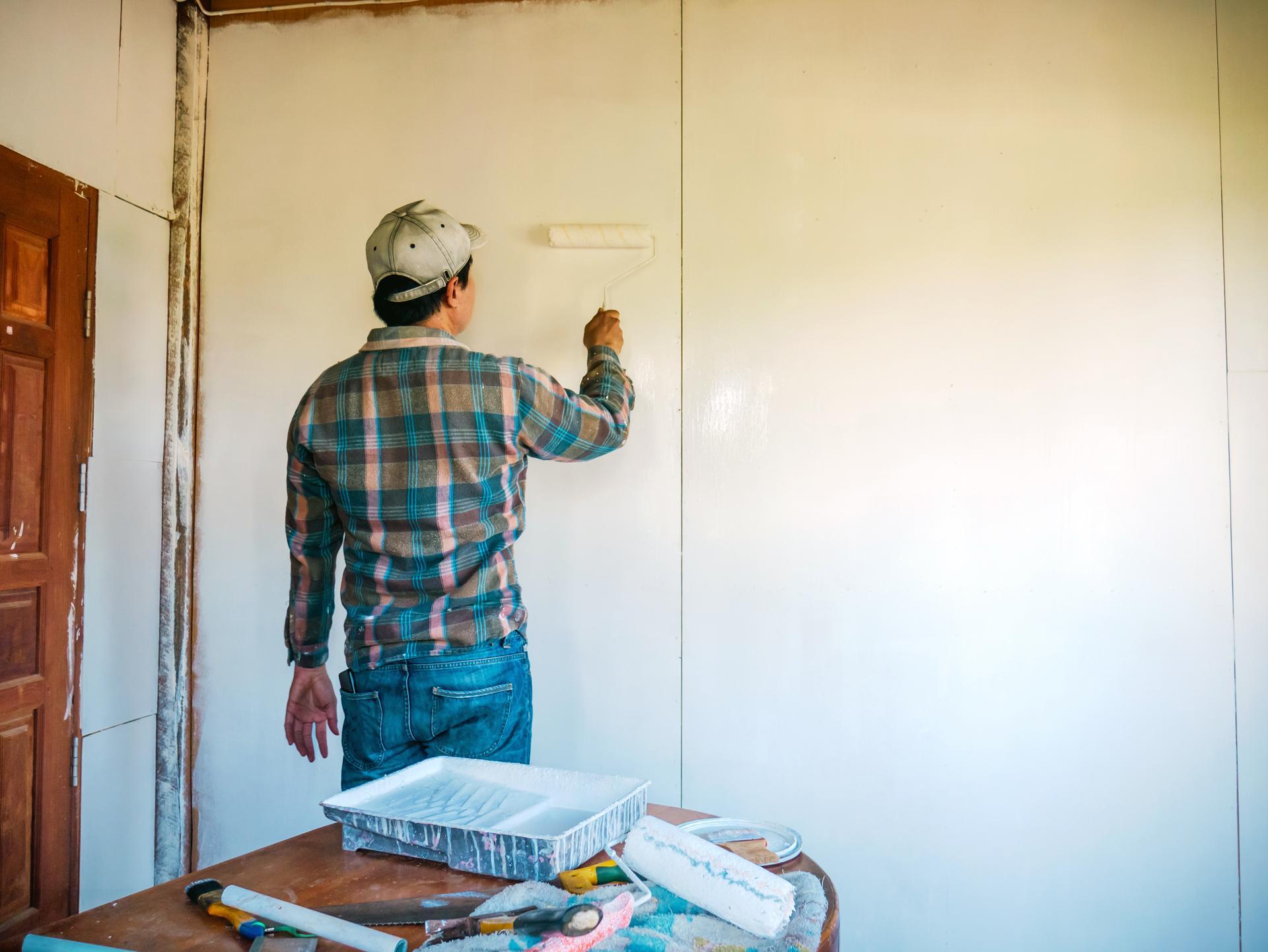 Back view of Workers painter are painting the wooden walls of the room white with paint roller,improvement home interior concept.