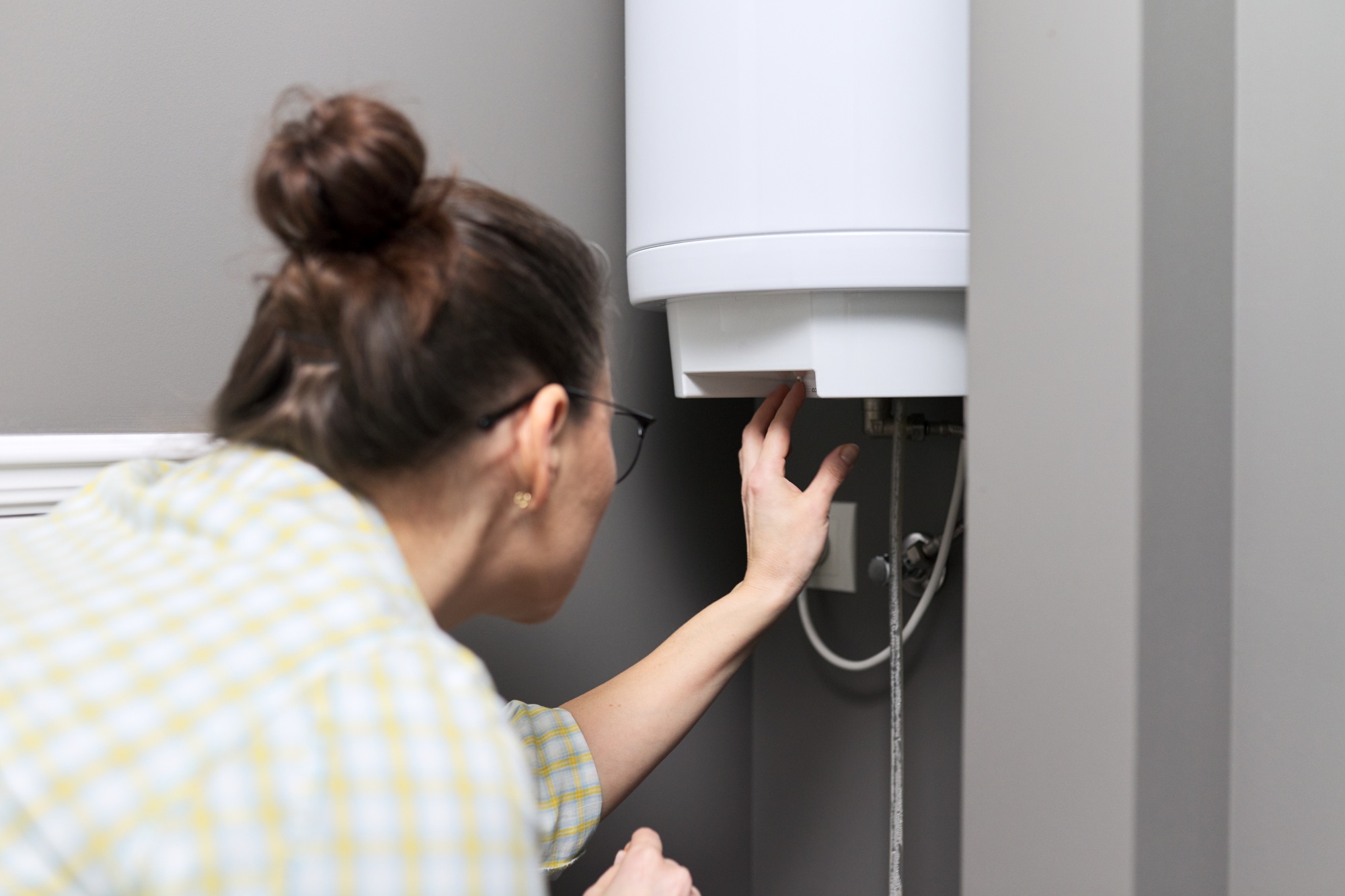 Plumbing and HVAC Resources 5 Home water heater, woman regulates the temperature on an electric water heater