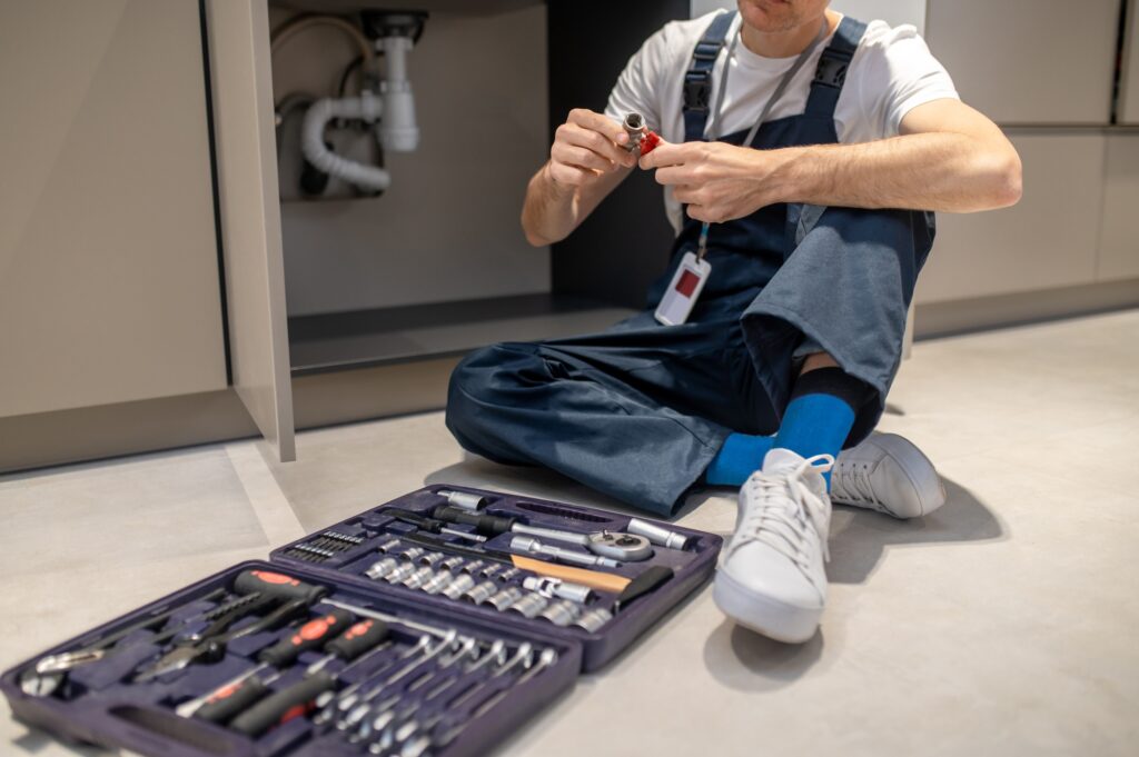 Noisy Pipes: What’s Normal and What’s Not 2 Man sitting on floor with plumbing detail in hands